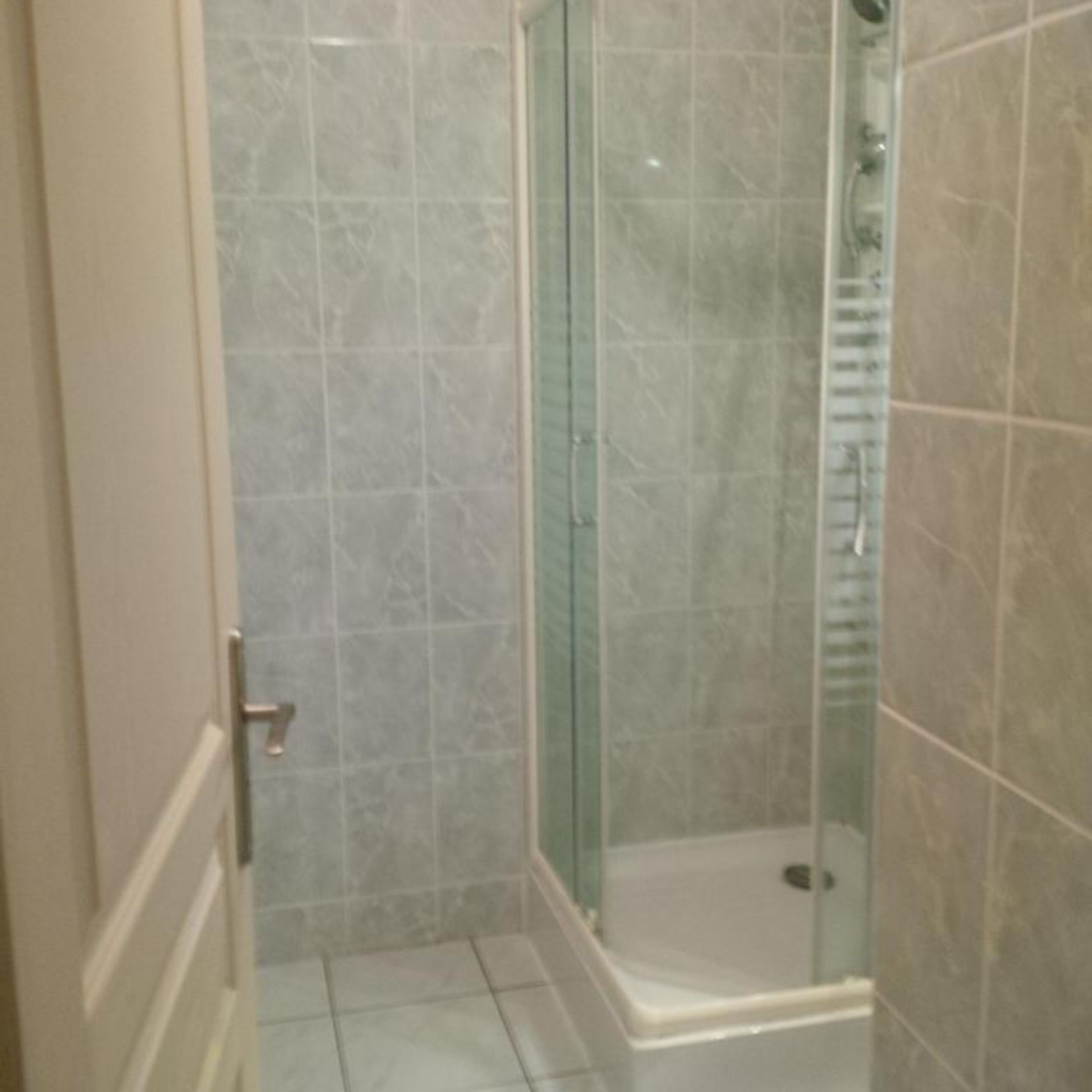 A bathroom with a glass shower enclosure, tiled walls, and a white floor.