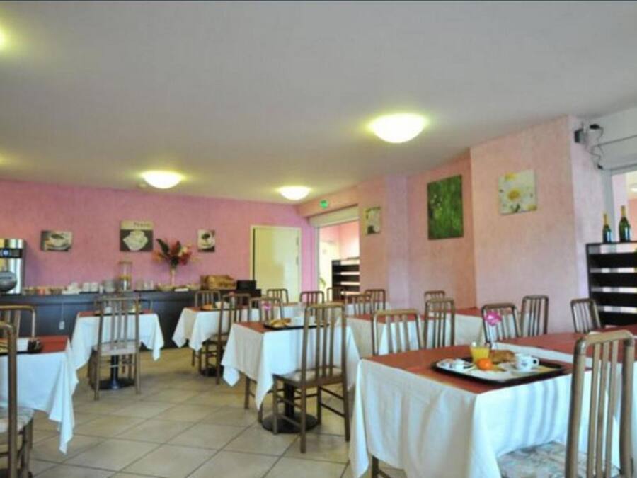 Un coin repas avec des tables préparées pour le petit-déjeuner, agrémenté d’un mur rose et de luminaires au plafond.