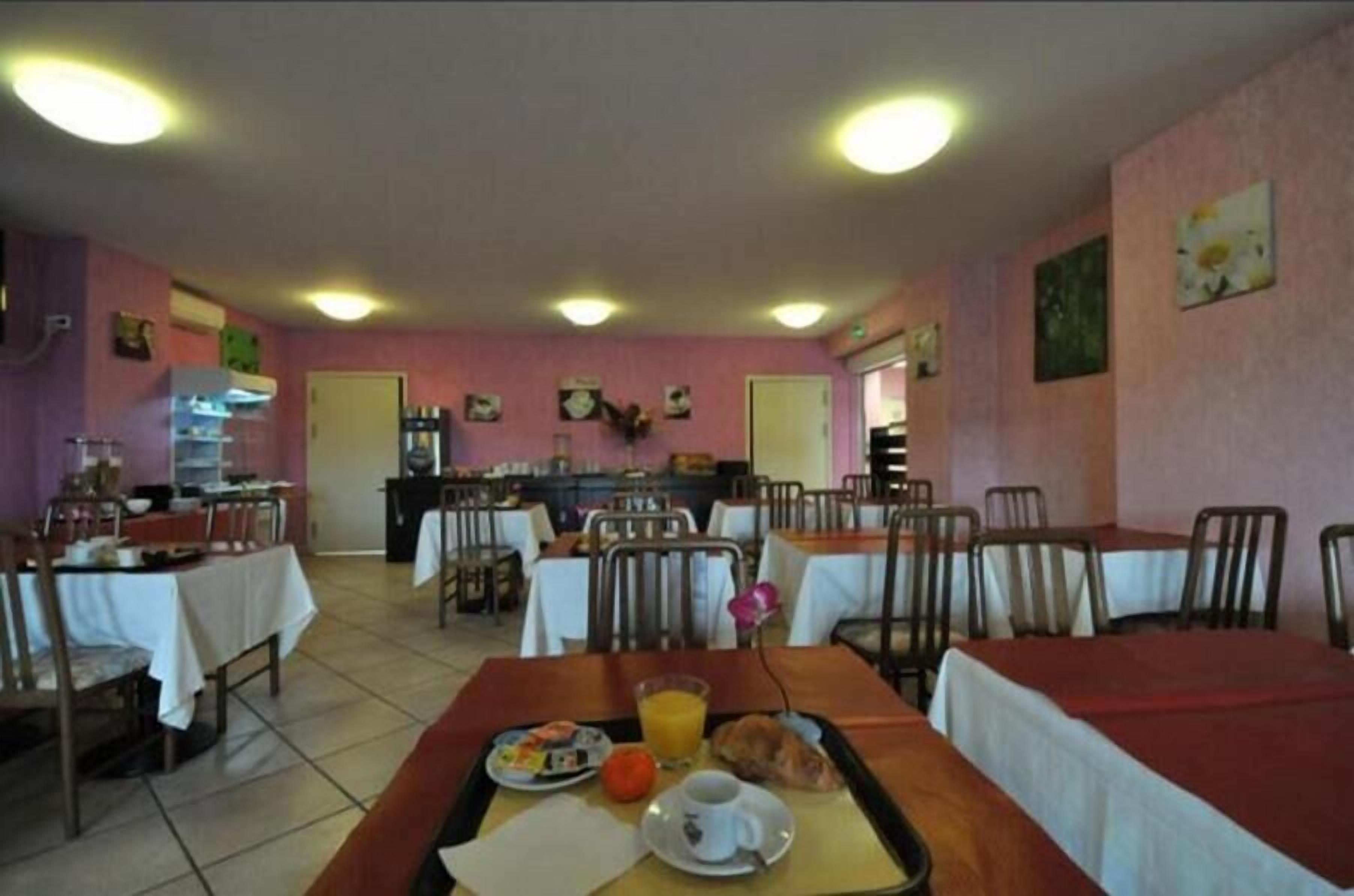 Un espace repas avec des tables et des chaises, une cuisine à l’arrière-plan et un mur rose orné d’œuvres d’art.