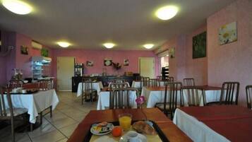 Un espace repas avec des tables et des chaises, une cuisine à l’arrière-plan et un mur rose orné d’œuvres d’art.