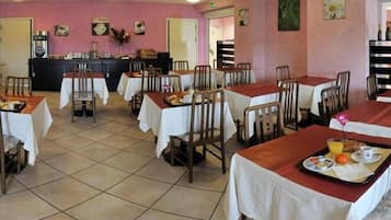 A dining area with tables set for breakfast, a coffee machine, and a counter with food items.