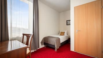 Een hotelkamer met een bed, een houten bureau, een stoel, een rood tapijt en een houten deur.