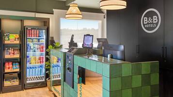 A B&B hotel reception area with a green tiled counter, a beverage vending machine, and a large window offering a view.