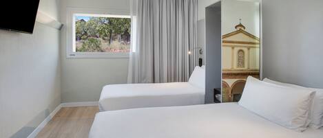 A hotel room with two beds, a window with curtains, a flat-screen TV mounted on the wall, and a painting of a building on the wall.