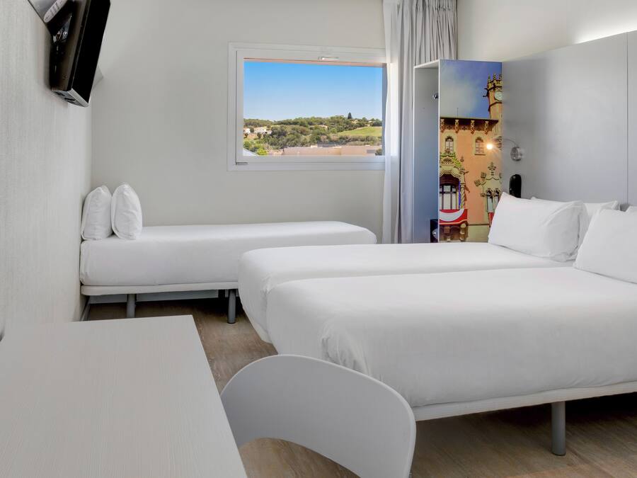 Une chambre d’hôtel avec deux lits simples, un bureau et une chaise. Il y a une fenêtre donnant sur un paysage verdoyant et des bâtiments.