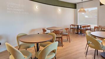 A modern dining area with round tables and chairs, a projection screen on the wall, and large windows allowing natural light.