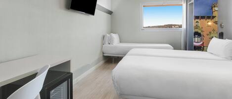 A hotel room with two beds, a TV mounted on the wall, a window with a view of the city, and a desk with a chair.