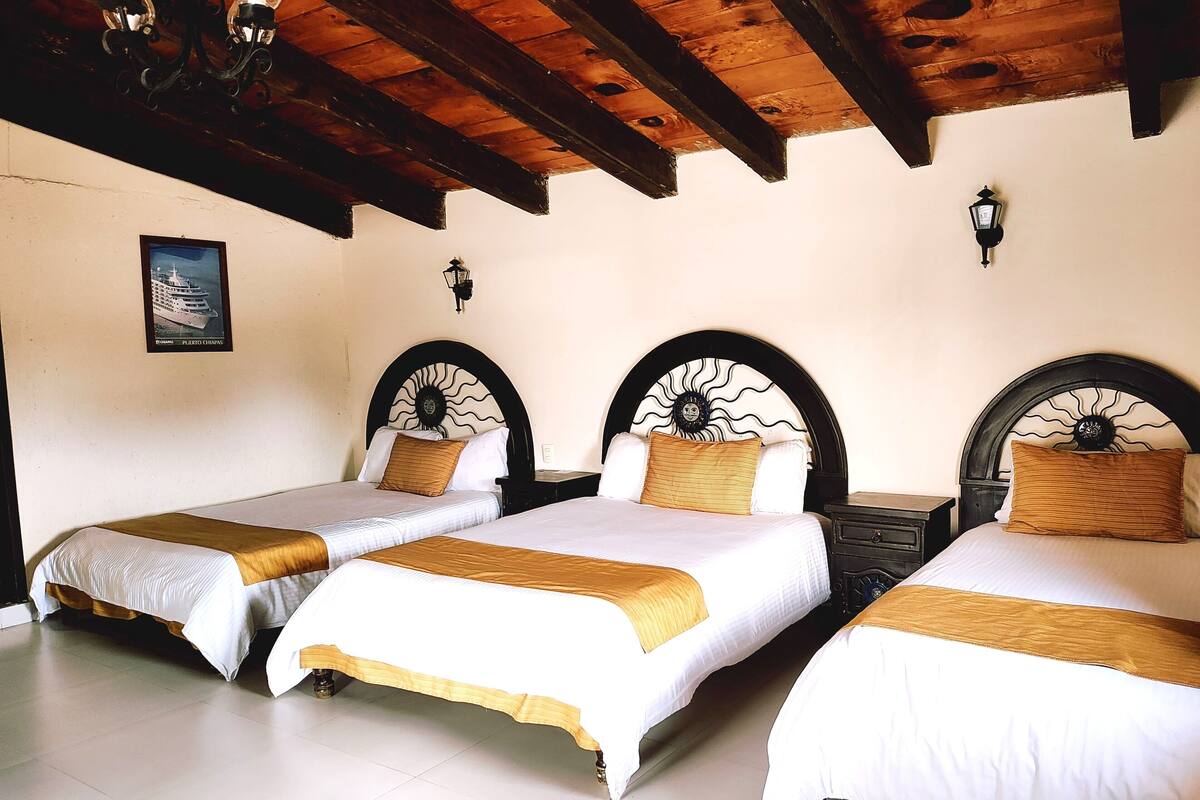 Ein Hotelzimmer mit drei Betten, Holzbalken an der Decke und einem gerahmten Bild an der Wand.