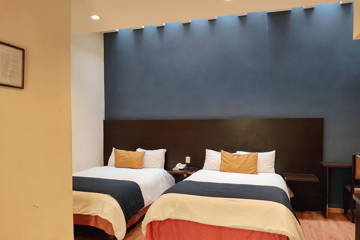 Ein Hotelzimmer mit zwei Betten, Holzboden und einem dunkelbraunen Kopfteil.