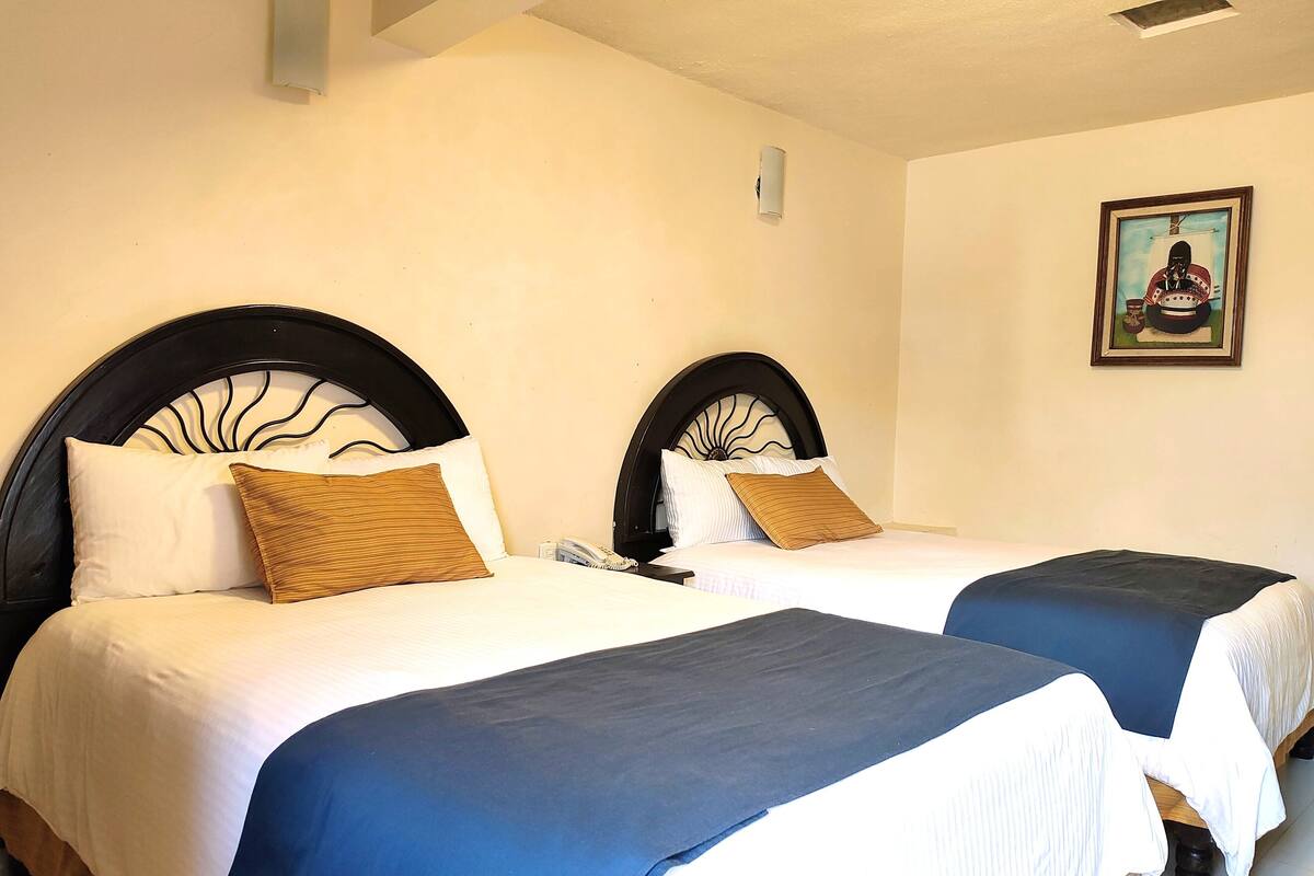 Ein Hotelzimmer mit zwei Betten, jeweils mit schwarzem Kopfteil und weißer Bettwäsche. An der Wand hängt ein Gemälde und auf dem Nachttisch steht ein Telefon.
