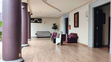 A spacious lobby with a grey sofa, purple chairs, and a large plant.