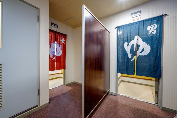 A hallway with a sliding door, a red curtain with a white symbol, and a blue curtain with a white symbol.