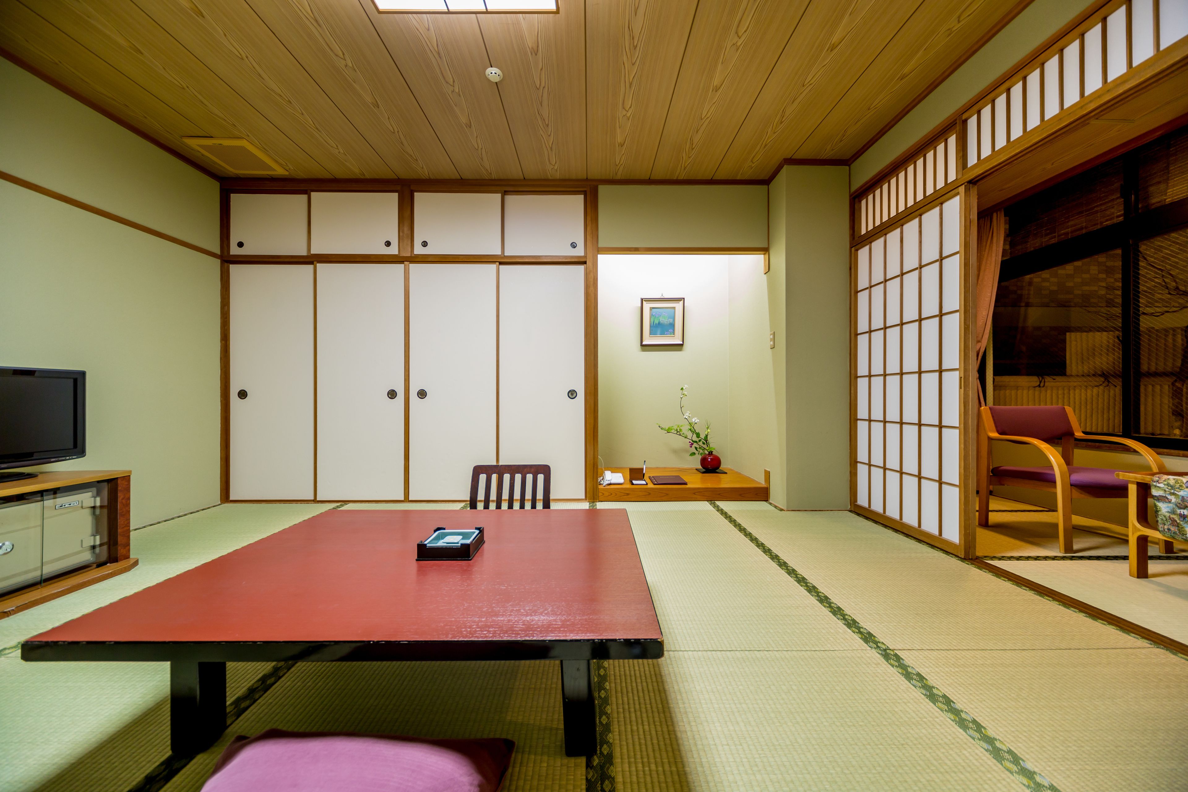 Una habitación japonesa tradicional con suelo de tatami, una mesa baja, un televisor y puertas correderas.