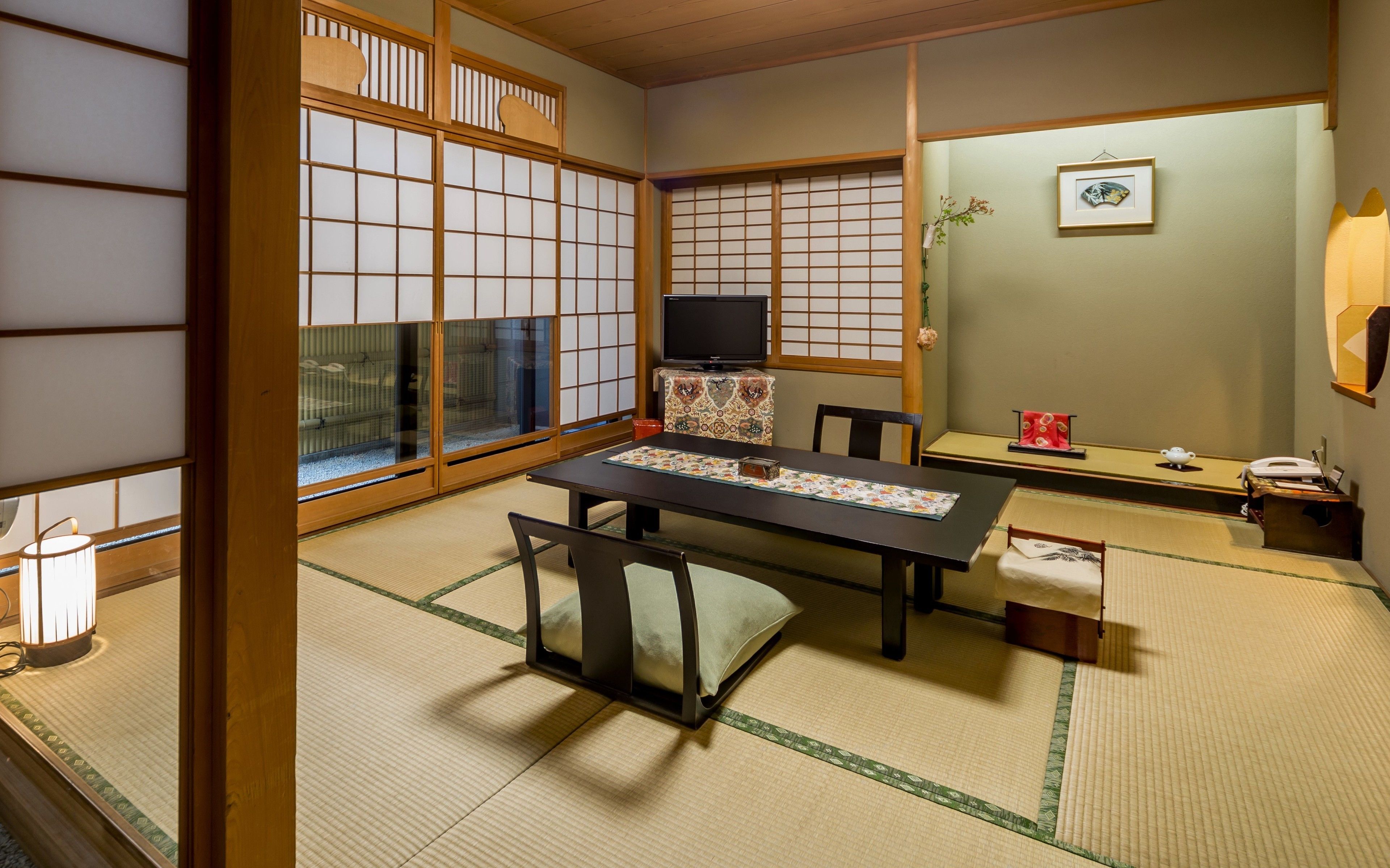 Una habitación japonesa tradicional con suelo de tatami, una mesa baja y un televisor sobre un mueble.