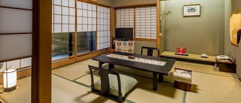 Una habitación japonesa tradicional con suelo de tatami, una mesa baja y un televisor sobre un mueble.