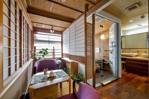 Una habitación tradicional japonesa con suelo de tatami, un panel shoji, una puerta de vidrio corredera que da a un baño y una mesa de madera baja con una silla morada.