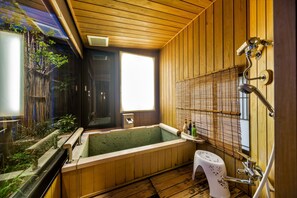 Una habitación tradicional japonesa con interiores de madera, una bañera para remojar y un ventanal pequeño.