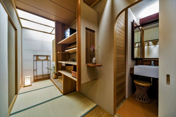 A traditional Japanese interior with tatami flooring, a wooden shelf with a vase, and a sink with a wooden stool.