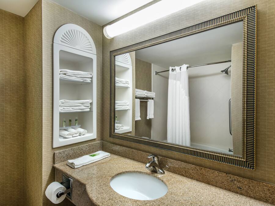 A bathroom with a sink, mirror, towel racks, and a shower curtain.