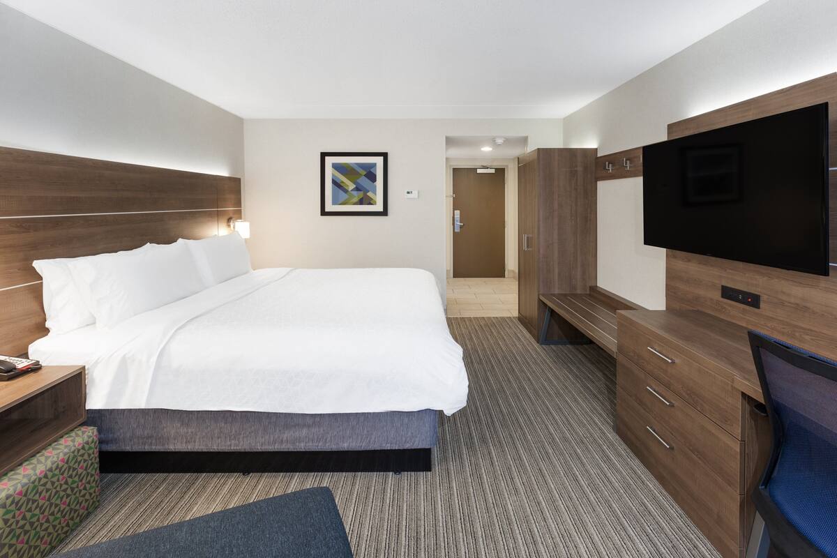 A hotel room with a large bed, a TV, a desk with a lamp, and a wardrobe.
