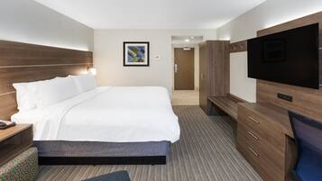 Quarto de hotel com uma cama grande, televisão, escrivaninha com candeeiro e guarda-roupa.