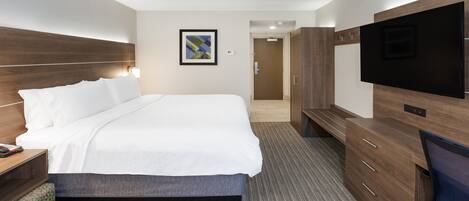 A hotel room with a large bed, a TV, a desk with a lamp, and a wardrobe.