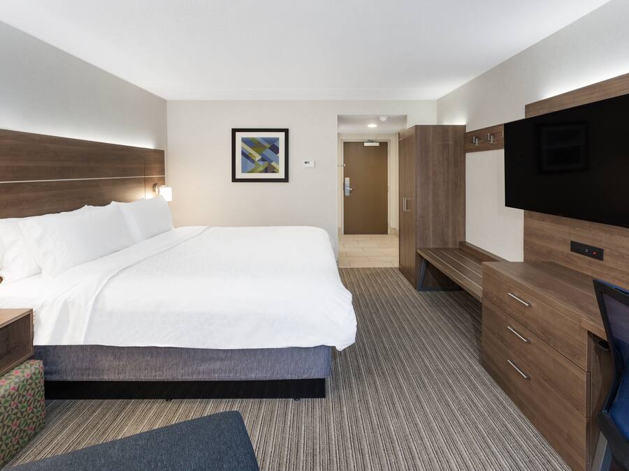 Quarto de hotel com uma cama grande, televisão, escrivaninha com candeeiro e guarda-roupa.