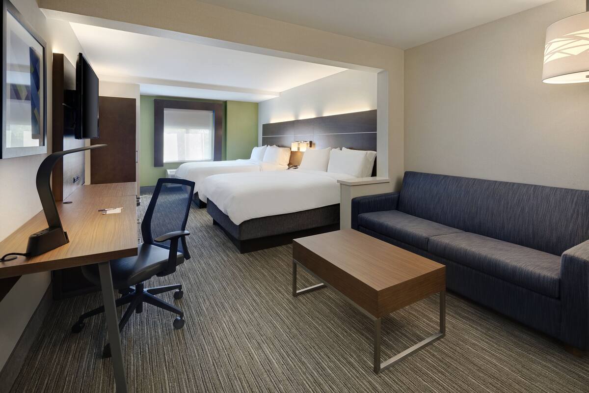 A hotel room with a bed, a desk with a chair, a sofa, and a TV mounted on the wall.