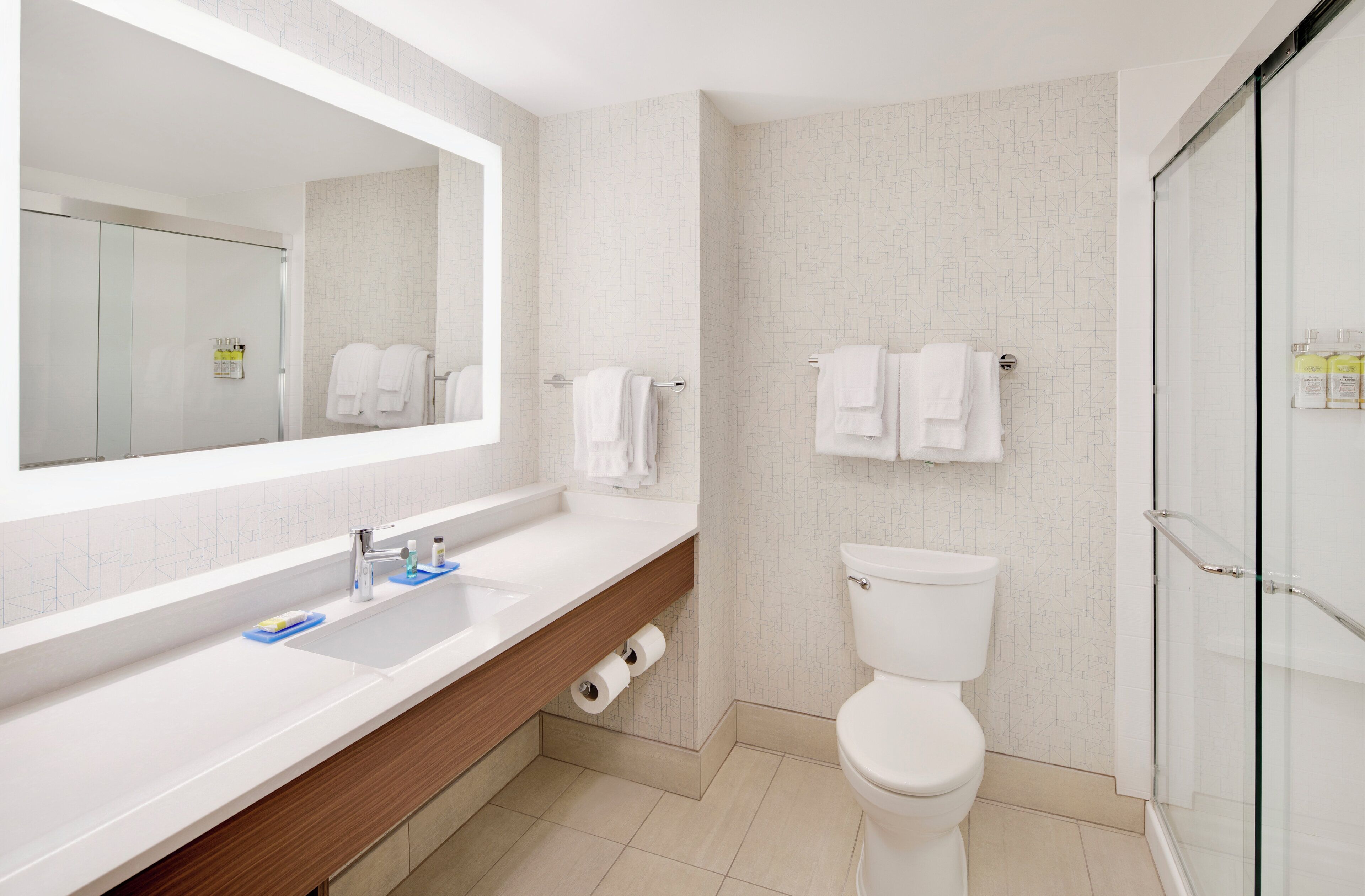A modern bathroom with a large mirror, a white sink, a toilet, and a glass shower enclosure.