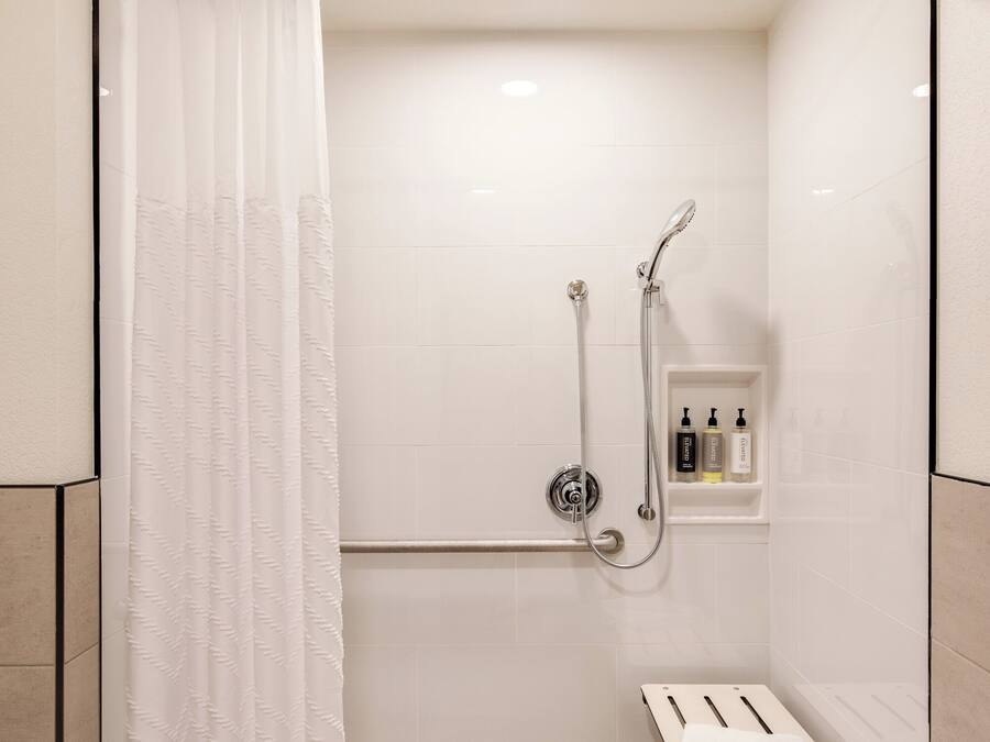A modern shower area with a glass door, a handheld showerhead, a wall-mounted faucet, and a small shelf with toiletries.