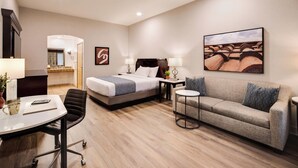Habitación de hotel con cama, sofá, escritorio con silla, una mesita y un cuadro en la pared.
