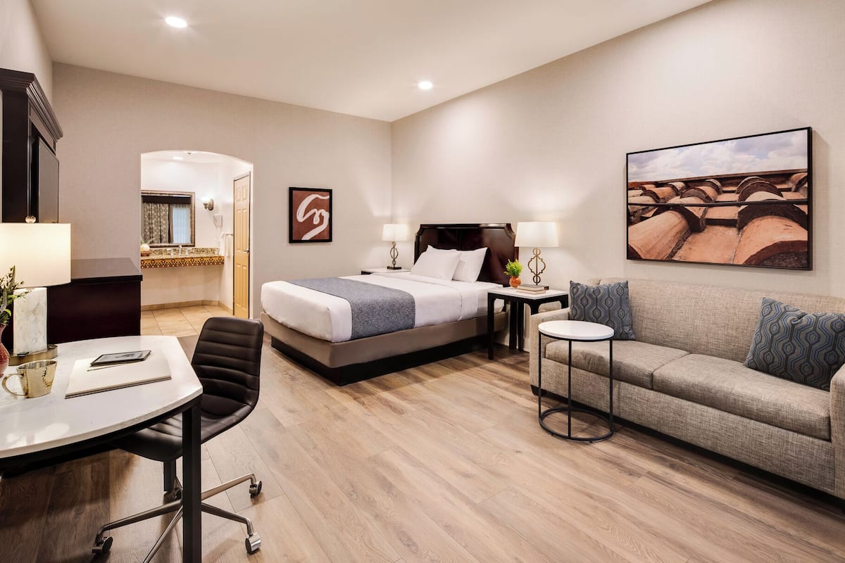 Habitación de hotel con cama, sofá, escritorio con silla, una mesita y un cuadro en la pared.