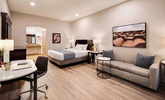 Habitación de hotel con cama, sofá, escritorio con silla, una mesita y un cuadro en la pared.