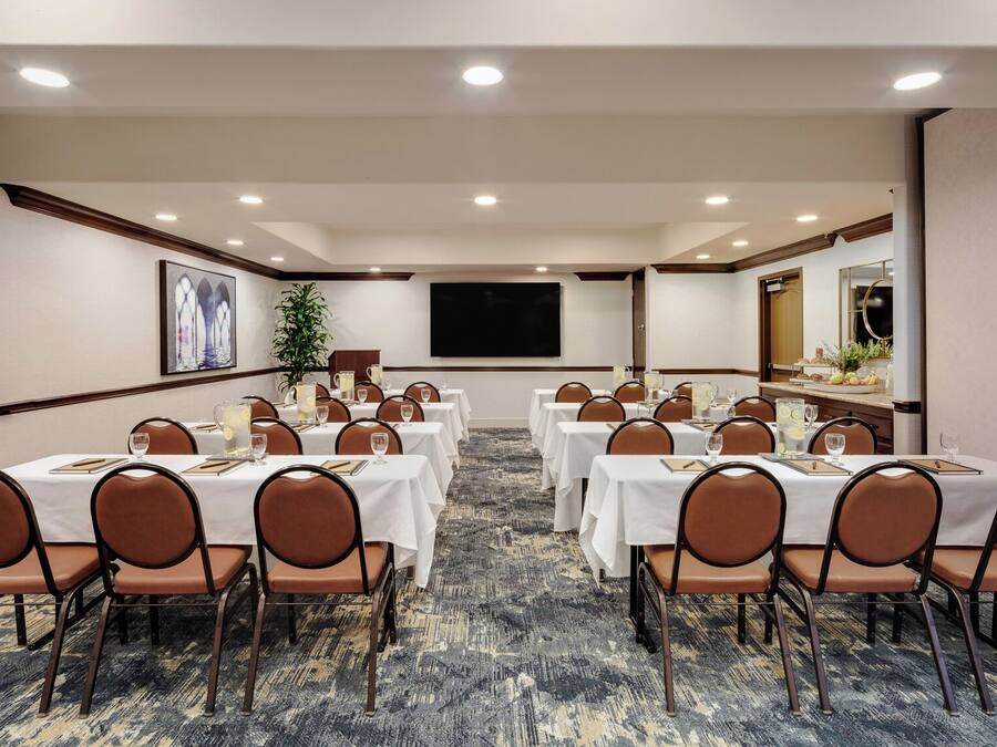 A conference room with tables and chairs, a large screen, and a plant.
