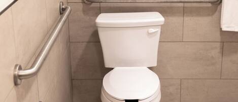 A bathroom with a white toilet, a handrail, and a towel rack.