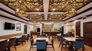 Un restaurante con techos altos, candelabros ornamentales y una zona de cocina central.