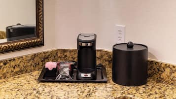 Una encimera de cocina con una cafetera, un hervidor y un soporte para cápsulas de café.