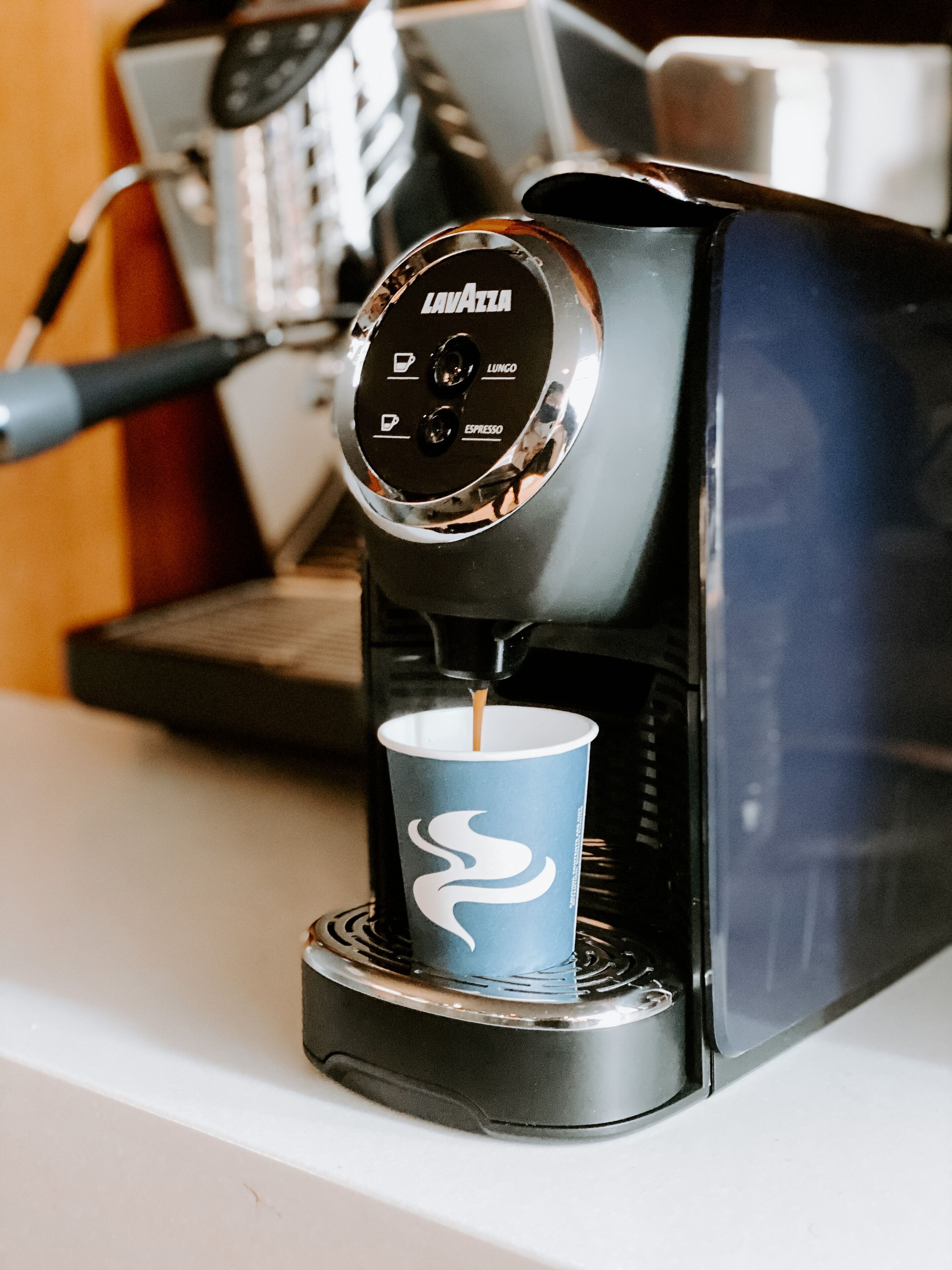 Una máquina de café vertiendo espresso en un vaso de papel.