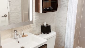 A modern bathroom with a white sink, a mirror, a toilet, and a shelf above the toilet.