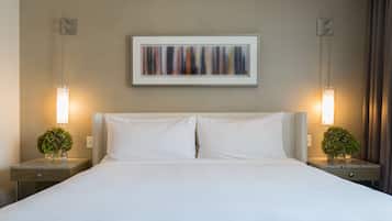 Een hotelkamer met een groot bed, twee nachtkastjes met lampen, een lijst met abstract kunstwerk aan de muur, en een klein plantje op elk nachtkastje.