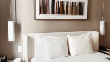 Habitación de hotel con una cama grande, una mesita de noche con un teléfono y una taza, y un cuadro abstracto colgado en la pared.