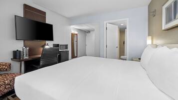A hotel room with a large bed, a flat-screen TV, a desk with a computer, and a bathroom visible through an open door.