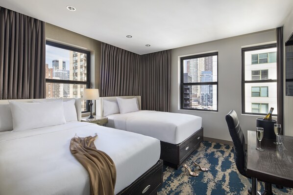 Habitación de hotel con dos camas, una mesa de comedor con sillas, vistas a la ciudad y un minibar.