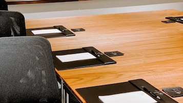 Una sala de conferencias con una larga mesa de madera, sillas negras y carpetas negras sobre la mesa.