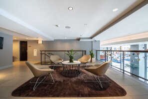 A modern lobby with a brown rug, a round table with chairs, and a potted plant. - Hotel Felix River North/Magnificent Mile (Chicago)