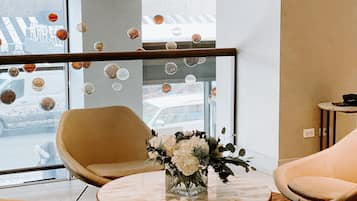 A modern hotel room with a round marble table, two beige armchairs, and a glass partition with bubble decorations.