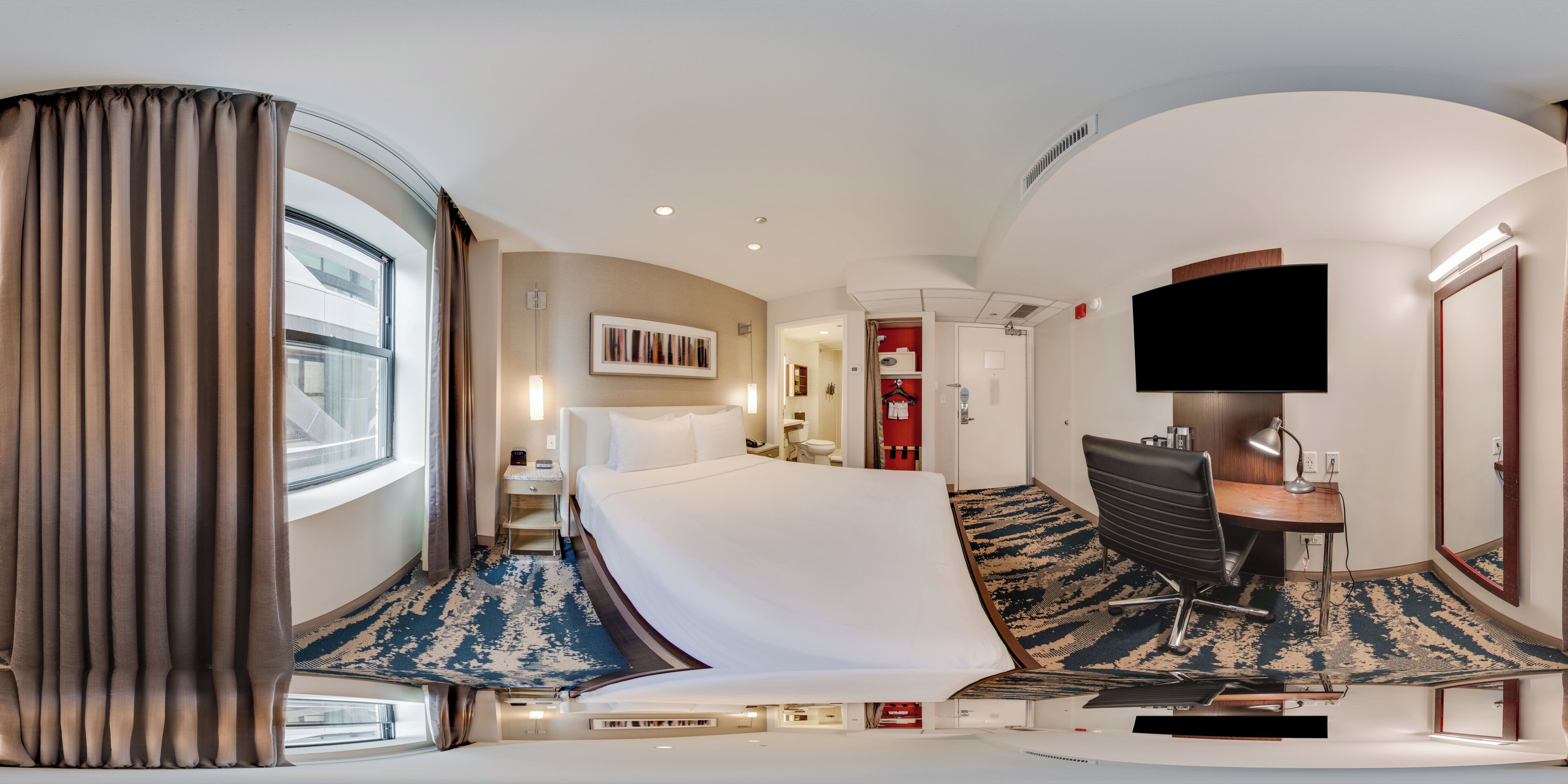 Una habitación de hotel con cama, escritorio, televisión y baño.