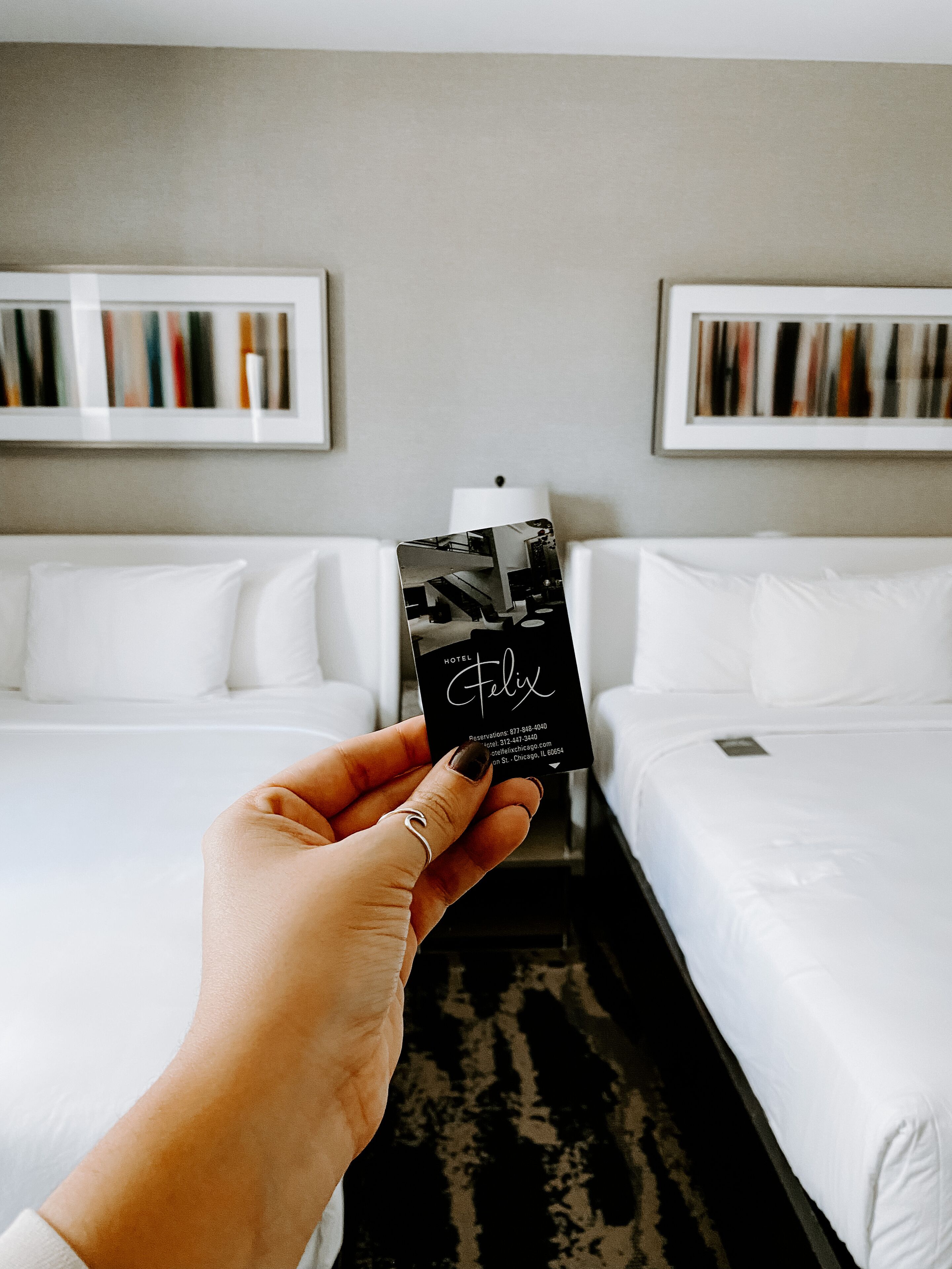 Una mano sosteniendo una tarjeta de reserva de Hotel Felix. En el fondo, dos camas blancas con ropa de cama blanca.