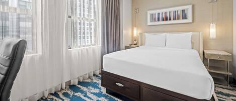 A hotel room with a bed, a chair, a nightstand, a lamp, and a painting on the wall.