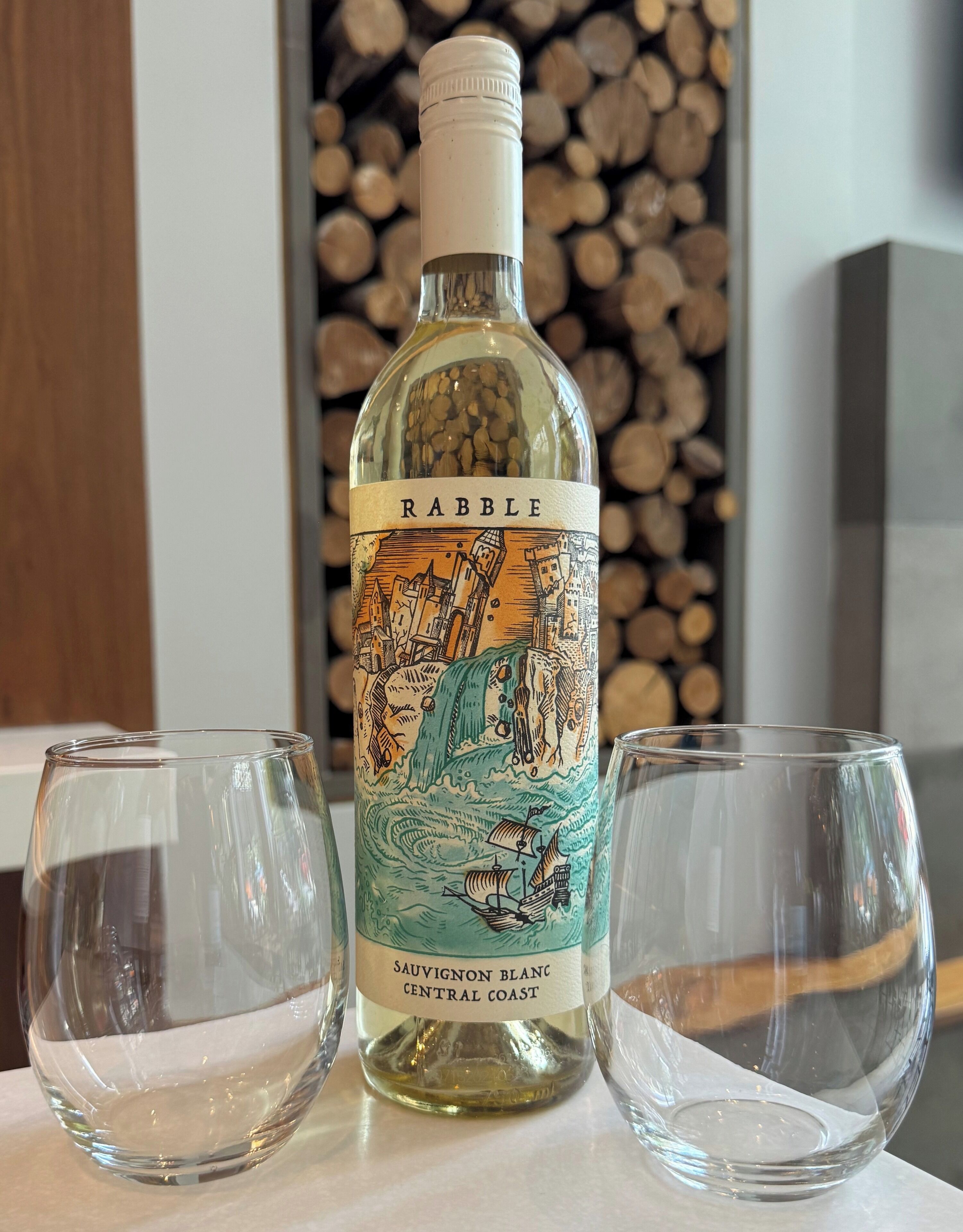 Una botella de vino blanco Sauvignon Blanc RABELLE, cosecha Central Coast, con dos copas de vino vacías a su lado.